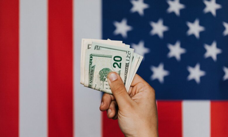 crop person showing pack of dollars against american flag