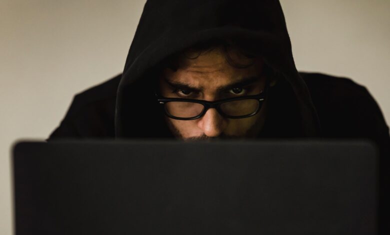 crop focused hacker in hood using laptop