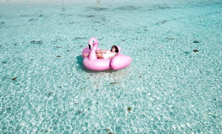 woman lying on pink flamingo bouy on body of water